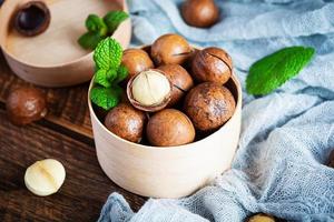 Noix de macadamia en coquille avec des feuilles de menthe et du miel sur fond de bois photo