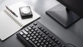 mise au point sélective sur un clavier noir avec une partie d'écran d'ordinateur, un stylo à bille, une montre de poche en cuir de voyage vintage et un carnet à spirales sur une table grise avec lumière du soleil et ombre sur la surface photo