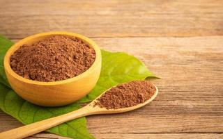 gros plan de poudre de cacao dans un bol en bois et une feuille verte sur une table en bois photo