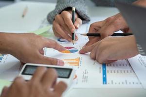 une équipe d'hommes d'affaires planifie avec leurs ordinateurs portables et leurs graphiques leurs bénéfices et utilise une calculatrice pour calculer le solde annuel de leur entreprise. photo