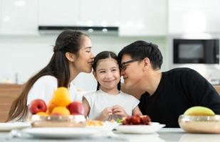 père et mère asiatiques montrent votre amour à la petite fille et prennent le petit déjeuner ensemble joyeusement dans la salle à manger de la maison. photo