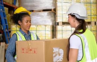 deux filles employées d'entrepôt s'entraident pour soulever de lourdes boîtes pour déplacer le stockage. photo