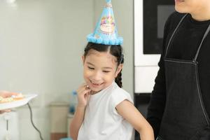 une famille asiatique de nouvelle génération cuisine ensemble et organise une petite fête d'anniversaire pour notre petite fille dans la cuisine de la maison photo