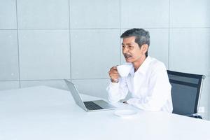 vieil homme d'affaires asiatique avec une chemise blanche travaillant et buvant du café dans la salle de réunion au bureau photo