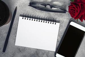 carnet de notes avec tasse à café jetable, stylo, smartphone et roses sur table en marbre. photo