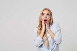 portrait d'une jolie femme blonde surprise avec des paumes sur ses joues, regardant de côté émerveillé par la bouche grande ouverte, debout sur fond blanc photo