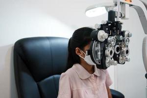 ophtalmologiste examinant les yeux d'une fille asiatique dans une clinique. ils portent des masques protecteurs.