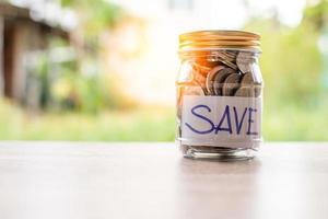 pièces de monnaie et texte sauvegardés dans un bocal en verre placé sur une table en bois. concept d'économiser de l'argent pour les investissements et les situations d'urgence. gros plan, arrière-plan flou photo