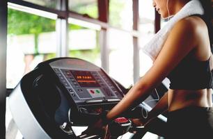 fille dans la salle de gym travaillant sur un tapis roulant automatique utiliser un téléphone portable en écoutant de la musique avec des écouteurs blancs et en utilisant une minuterie de rythme cardiaque numérique. exercice systématique sa détente de vacances photo