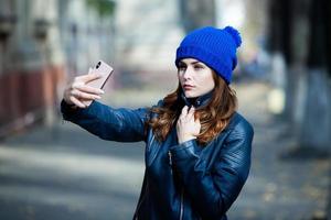 image de belle femme élégante tenant un téléphone portable. jeune fille européenne debout dans la rue et utilisant un téléphone portable. femme écoutant de la musique avec le téléphone et s'amusant. notion d'internet mobile. photo