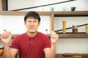 un jeune homme asiatique avec un t-shirt rouge décontracté aime prendre son petit déjeuner, manger des frites en riant. jeune homme cuisinant des aliments dans la salle de cuisine de style loft photo