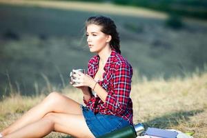 belle femme boit du thé à l'extérieur. femme hipster relaxante dans la nature photo