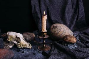 vieux crâne de chien, bougie allumée, runes en bois et pierres sur la table de sorcière. photo