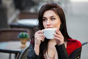 jeune femme élégante buvant du café dans une rue de la ville. fille hipster élégante buvant du café dans la rue. portrait de mode en plein air de jeune belle fille buvant du café. photo