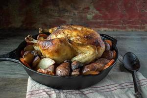 poulet entier cuit au four avec des légumes rôtis dans une poêle en fonte sur une table rustique photo