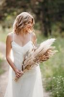 fille mariée heureuse dans une robe légère blanche avec un bouquet de fleurs séchées photo