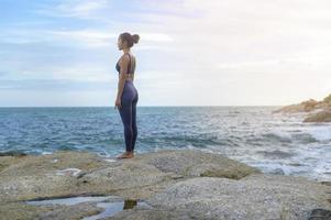 jeune femme asiatique en tenue de sport faisant du yoga sur le rocher au bord de la mer, concept de santé et de méditation