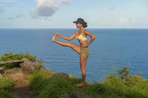 belle femme asiatique en vêtements de sport faisant du yoga sur le sommet de la montagne en bord de mer après le concept de trekking, de voyage et de méditation. photo