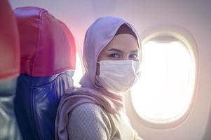 jeune femme musulmane avec hijab portant un masque facial à bord, nouveau voyage normal après le concept de pandémie de covid-19 photo