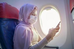 jeune femme musulmane avec hijab portant un masque facial à bord, nouveau voyage normal après le concept de pandémie de covid-19 photo