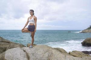 jeune femme asiatique en tenue de sport faisant du yoga sur le rocher au bord de la mer, concept de santé et de méditation