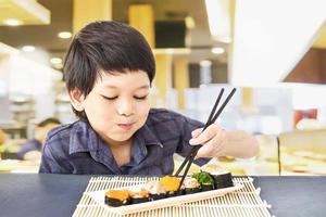 Un adorable garçon asiatique mange des sushis au restaurant photo