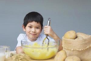 Garçon de 7 ans faisant de la purée de pommes de terre avec bonheur photo