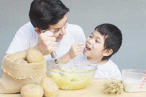 papa et fils faisant de la purée de pommes de terre avec bonheur photo