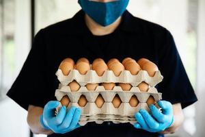un homme porte un plateau d'œufs à 3 couches pour rester en sécurité à la maison en mettant un gant sanitaire pendant la propagation du virus corona covid-19 - les gens gardent de la nourriture dans le concept de période de propagation virale covid-19. photo