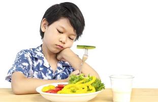 Adorable garçon asiatique montrant une expression ennuyeuse avec des légumes frais colorés et un verre de lait isolé sur fond blanc photo