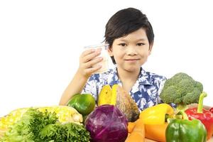 Garçon asiatique en bonne santé montrant une expression heureuse avec un verre de lait et une variété de légumes frais colorés sur fond blanc photo