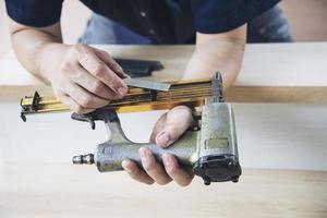 Charpentier à l'aide d'un pistolet à air comprimé faisant des travaux de meubles en bois photo