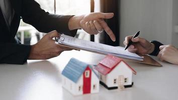 agent immobilier avec un modèle de maison mettant à la main un contrat de signature, ayez un contrat en place pour le protéger, signature d'accords modestes au bureau. concept immobilier, déménagement ou location de propriété photo