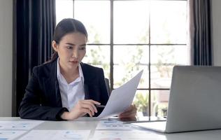 portrait d'une femme asiatique travaillant sur une tablette dans un bureau moderne. faire un rapport d'analyse de compte. information sur l'investissement immobilier concepts du système financier et fiscal photo