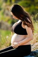 femme enceinte avec de longs cheveux sains et des fleurs. belle fille attendant le bébé. la future mère serre son ventre. photo