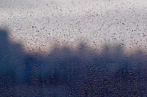 goutte de pluie sur la fenêtre en verre pendant la saison de la mousson avec un arrière-plan flou de la ville. photo