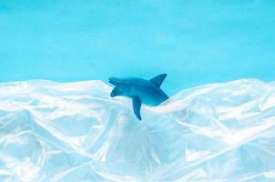 un modèle de jouet de requin emprisonné dans un sac en plastique blanc sur fond bleu. concept de monde océanique minimal. photo