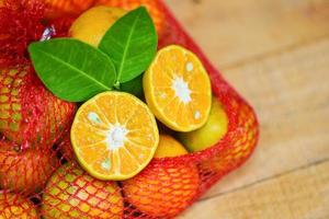 fruit orange dans un sac sur fond de bois - tranche d'orange fraîche moitié et feuille d'orange concept de récolte de fruits sains photo