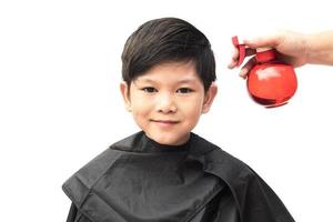 un garçon est pulvérisé ses cheveux par coiffeur isolé sur fond blanc photo