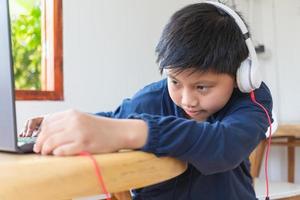 un joli garçon asiatique tend la main pour brancher lui-même ses écouteurs sur son ordinateur portable avec un visage qui a l'intention d'utiliser l'ordinateur pour étudier en ligne à la maison. lier et connecter photo
