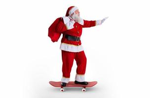 le père noël chevauchant un skateboard ou un longboard et tenant un sac plein de cadeaux sur fond blanc. photo