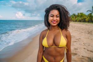 belle femme latino-américaine en bikini sur la plage. jeune femme profitant de ses vacances d'été par une journée ensoleillée, souriant et regardant la caméra photo