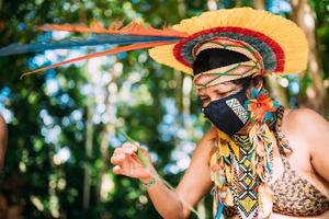 indien de la tribu pataxo avec une coiffe en plumes et un masque de protection contre la pandémie de covid-19. femme indigène du brésil faisant de l'artisanat photo