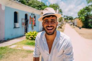 touriste faisant du selfie dans le centre historique de porto seguro. homme latino-américain au chapeau souriant à la caméra photo