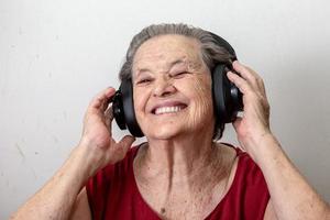 drôle de vieille dame écoutant de la musique et dansant sur fond blanc. femme âgée portant des lunettes dansant sur de la musique écoutant sur ses écouteurs. photo