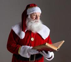 père noël avec un vieux livre à couverture rouge. griffonner des noms de cadeaux pour Noël. Noël approche photo