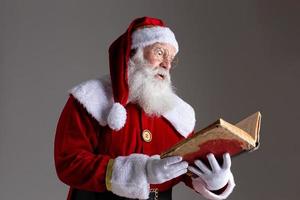 père noël avec un vieux livre à couverture rouge. griffonner des noms de cadeaux pour Noël. Noël approche photo