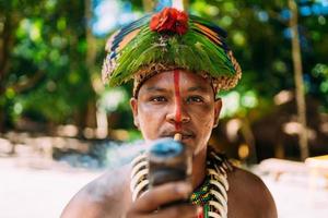 chef indien de la tribu pataxo fumant la pipe . indien brésilien avec coiffe de plumes et collier regardant la caméra photo
