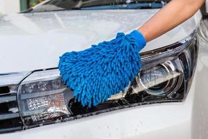 main de femme avec tissu en microfibre bleu phare de lavage voiture moderne ou automobile de nettoyage. concept de lavage de voiture photo