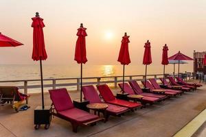 parasol rouge et chaises de piscine au lever du soleil autour de la piscine extérieure. photo